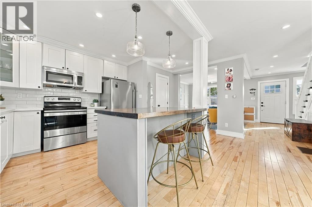 Kitchen featuring stainless steel appliances, white shaker-style cabinetry, subway tile backsplash, light wood flooring, and a central island with counter seating - 1231 Dunsmure Road, Hamilton, ON