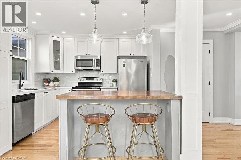 Bright kitchen featuring stainless steel appliances, white cabinetry, a subway tile backsplash, and a wood-finish island countertop - 1231 Dunsmure Road, Hamilton, ON