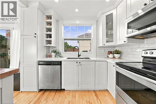 White shaker cabinetry, built-in wine rack, stainless steel appliances, solid surface countertops, and wood-finish flooring - 1231 Dunsmure Road, Hamilton, ON 