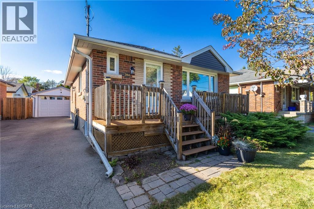 Brick exterior with siding accent, wood deck with railings, paved driveway, detached garage, and mature landscaping - 366 East 17Th Street, Hamilton, ON