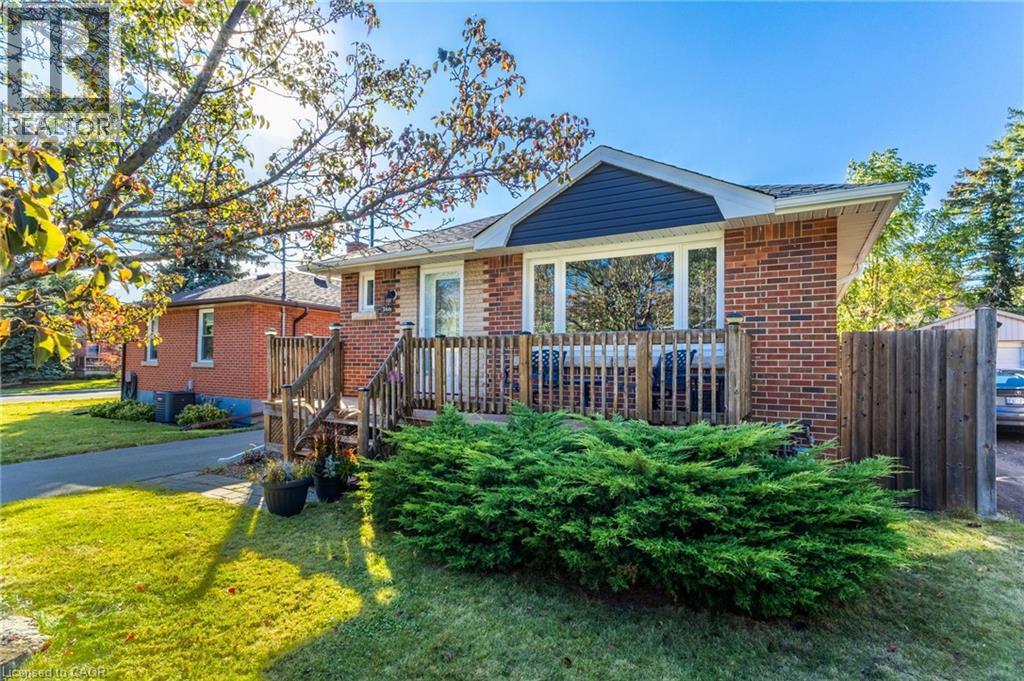 Brick exterior with a dark blue gable accent, front deck with wood railings, and a manicured lawn - 366 East 17Th Street, Hamilton, ON