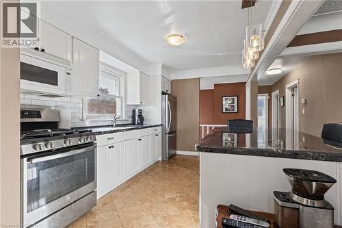 Kitchen featuring white cabinetry, stainless steel appliances, subway tile backsplash, and a breakfast bar with pendant lighting - 366 East 17Th Street, Hamilton, ON 