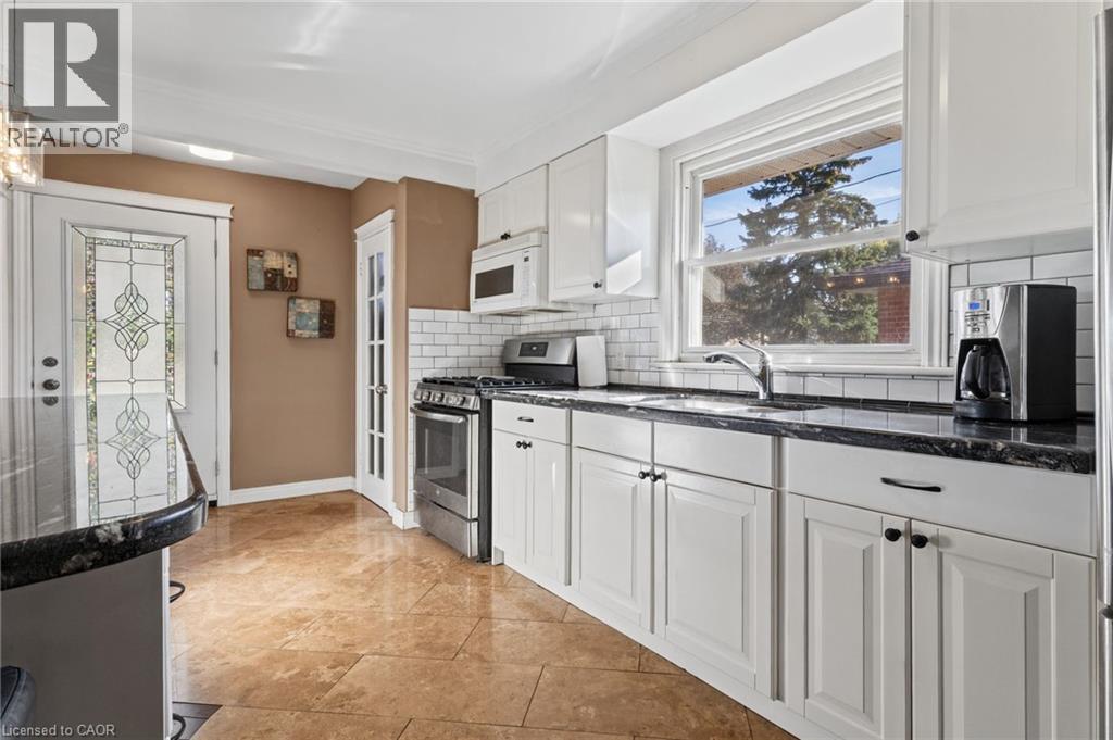 Kitchen featuring white cabinetry, dark stone countertops, stainless steel appliances, a white subway tile backsplash, and tile flooring - 366 East 17Th Street, Hamilton, ON