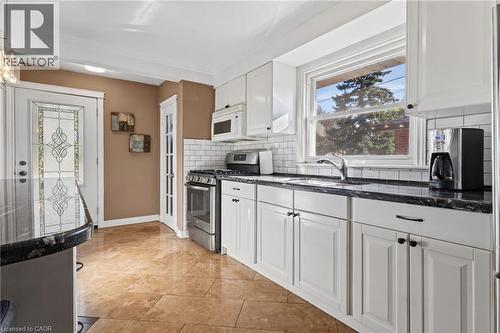 Kitchen featuring white cabinetry, dark stone countertops, stainless steel appliances, a white subway tile backsplash, and tile flooring - 366 East 17Th Street, Hamilton, ON 