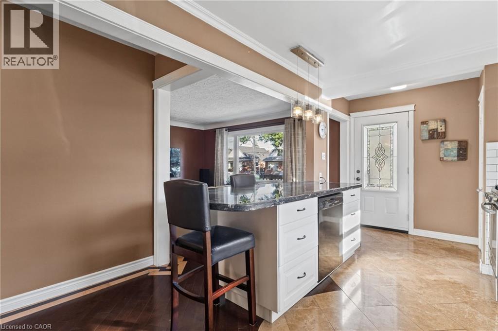 Kitchen island with a dark-toned countertop, white cabinetry with dark pulls, and a stainless steel dishwasher - 366 East 17Th Street, Hamilton, ON