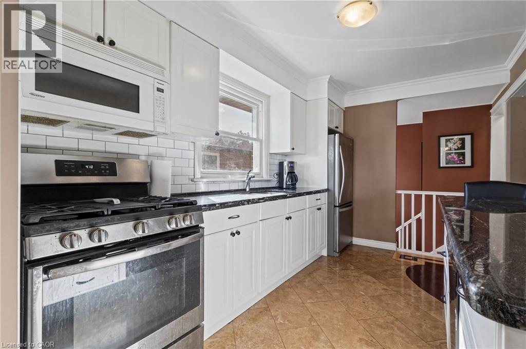 Kitchen featuring white cabinetry, subway tile backsplash, stainless steel appliances, dark countertops, and tile flooring - 366 East 17Th Street, Hamilton, ON