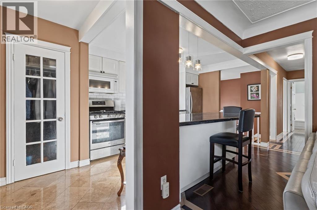 Sophisticated open-concept kitchen and dining area featuring warm taupe and white finishes, white cabinetry with glass-front doors, stainless steel built-in appliances, wood-finish flooring throughout - 366 East 17Th Street, Hamilton, ON