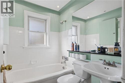 Full bathroom featuring a pedestal sink, white ceramic tiled walls, a bathtub with an integrated shower, and a mounted mirror - 366 East 17Th Street, Hamilton, ON 