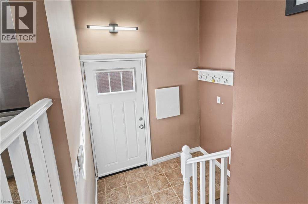 Entryway featuring a white paneled door with window inserts, tile flooring, and a modern wall-mounted light fixture - 366 East 17Th Street, Hamilton, ON