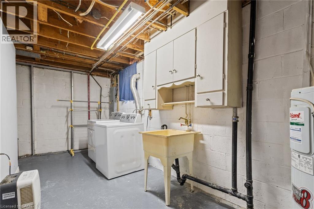 Utility area featuring white washer and dryer, laundry sink, and overhead cabinetry - 366 East 17Th Street, Hamilton, ON