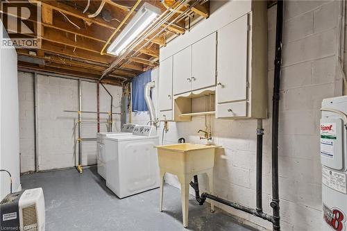 Utility area featuring white washer and dryer, laundry sink, and overhead cabinetry - 366 East 17Th Street, Hamilton, ON 