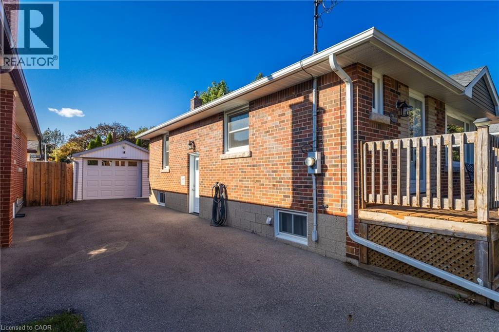 Red brick exterior with white trim, wood deck, asphalt driveway, and detached garage - 366 East 17Th Street, Hamilton, ON