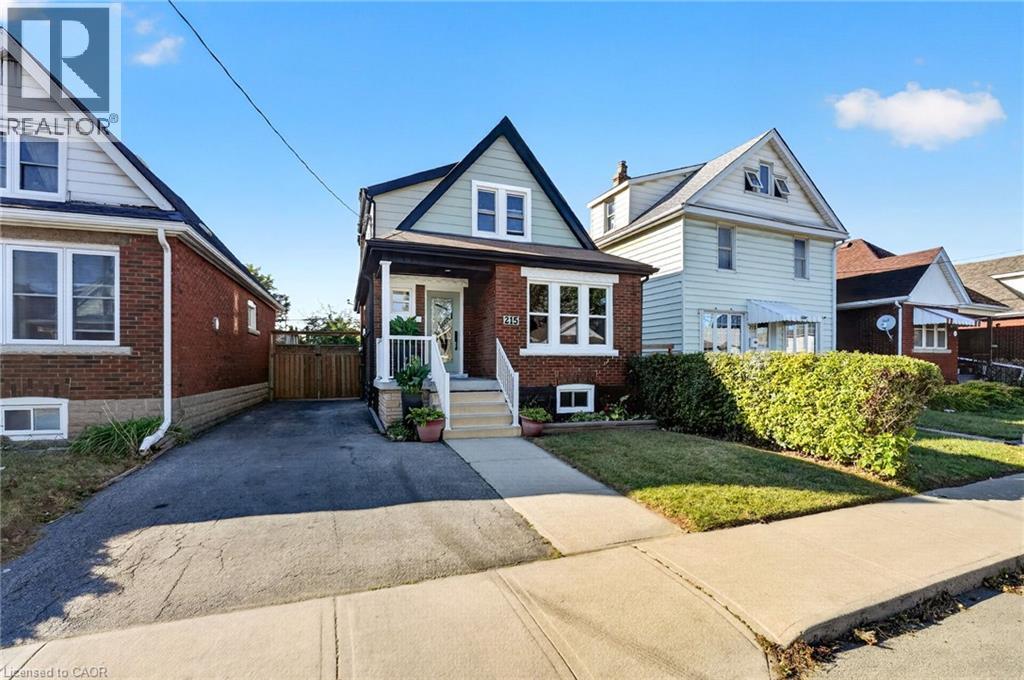 Brick facade with white trim, front porch with white railings, paved driveway, and a maintained front lawn - 215 Paling Avenue, Hamilton, ON