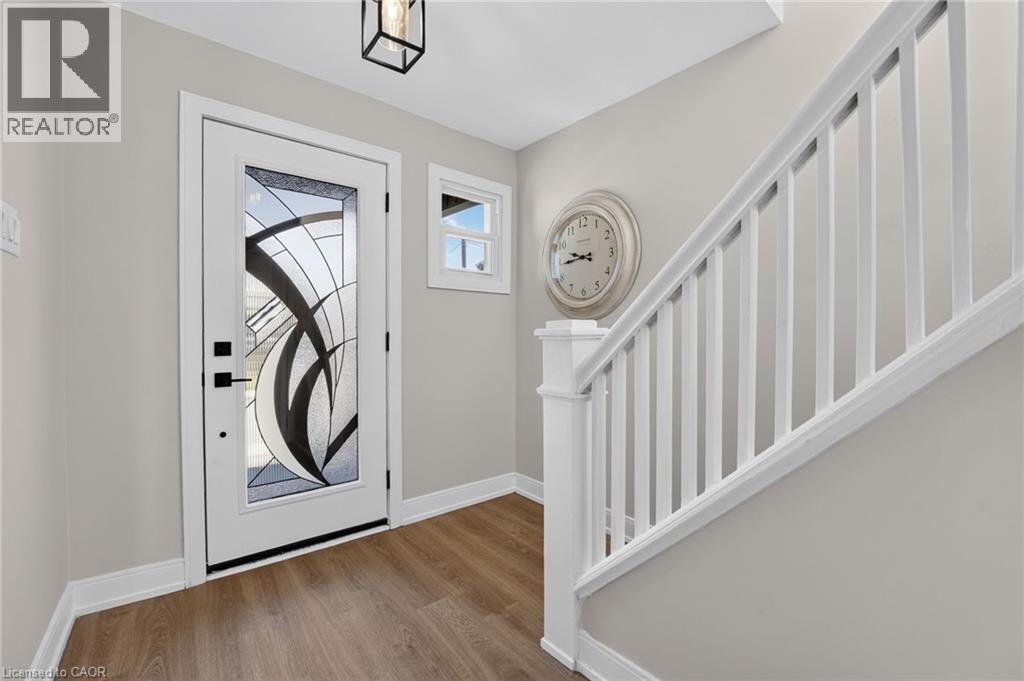 Entryway with a decorative glass front door, wood-finish flooring, a white-painted staircase, and a square ceiling light fixture - 215 Paling Avenue, Hamilton, ON