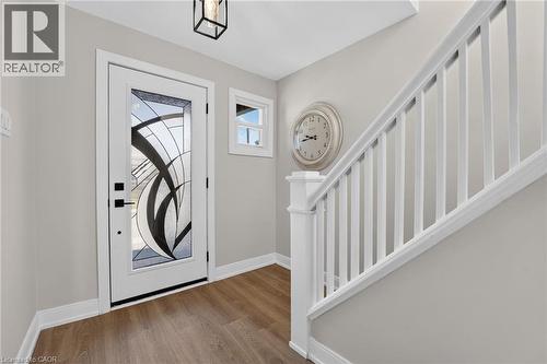 Entryway with a decorative glass front door, wood-finish flooring, a white-painted staircase, and a square ceiling light fixture - 215 Paling Avenue, Hamilton, ON 