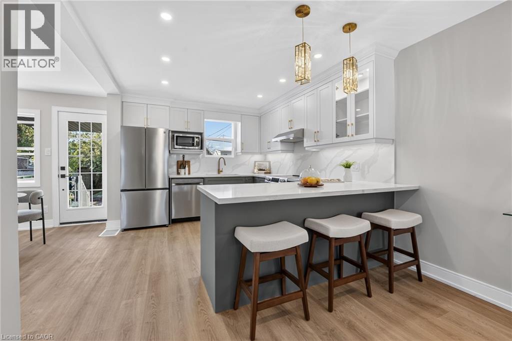Kitchen featuring light wood-finish flooring, white cabinetry with gold-toned hardware, stainless steel appliances, a white countertop, and two pendant light fixtures - 215 Paling Avenue, Hamilton, ON