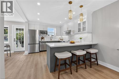 Kitchen featuring light wood-finish flooring, white cabinetry with gold-toned hardware, stainless steel appliances, a white countertop, and two pendant light fixtures - 215 Paling Avenue, Hamilton, ON 