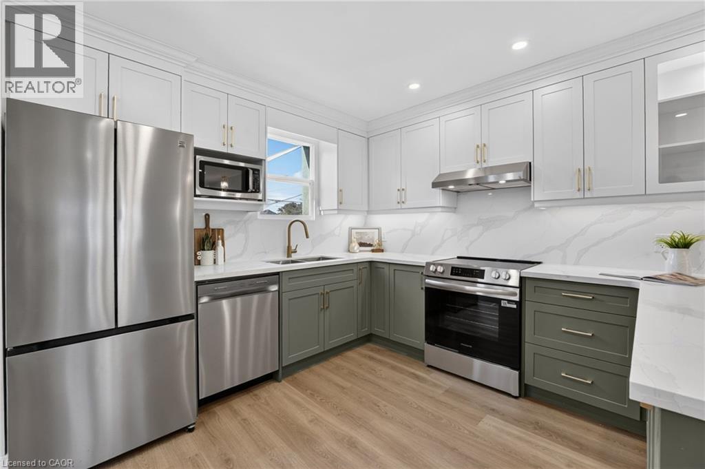 Kitchen featuring two-tone cabinetry, stainless steel appliances, white countertops, and a white backsplash with gray veining - 215 Paling Avenue, Hamilton, ON