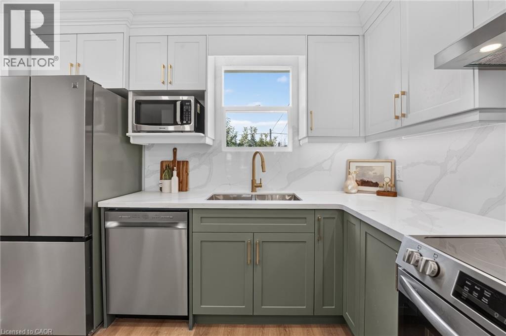 Two-tone cabinetry with gold-finish hardware, stainless steel appliances, white countertops, and a full-height backsplash - 215 Paling Avenue, Hamilton, ON