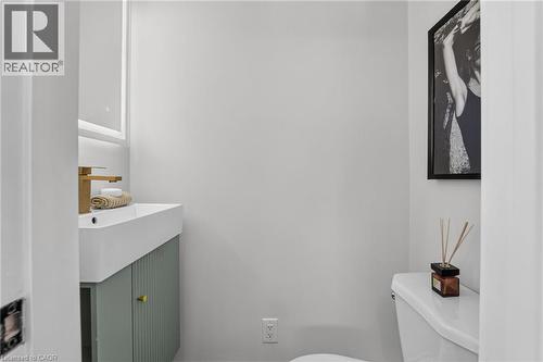 Wall-mounted rectangular sink with a gold-tone faucet, integrated vanity with fluted cabinetry, and an illuminated rectangular mirror - 215 Paling Avenue, Hamilton, ON 