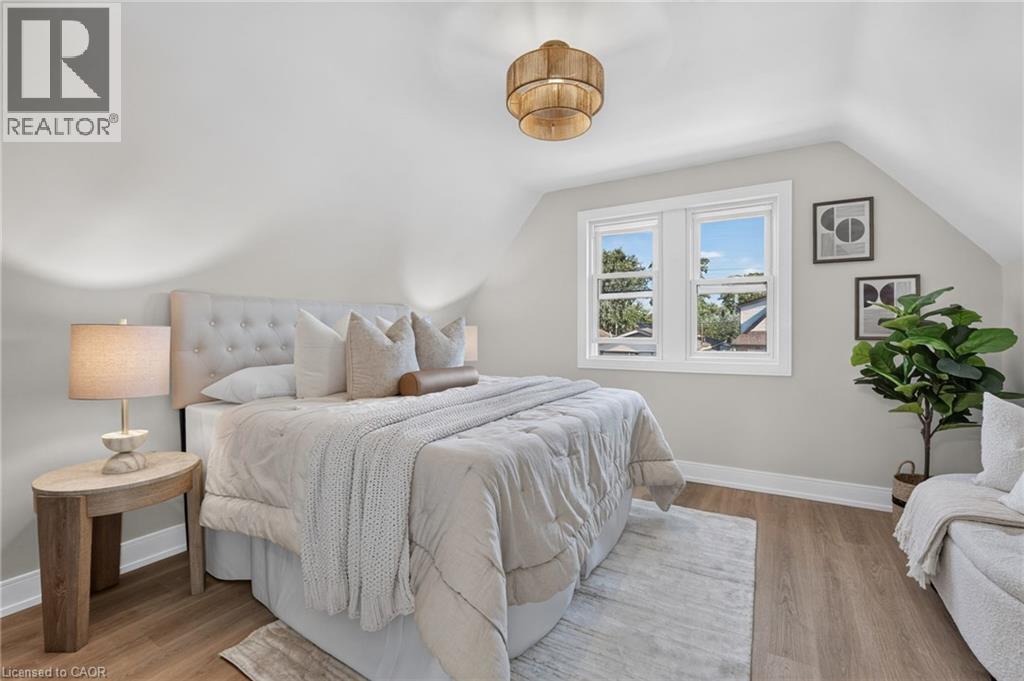 Sloped ceiling architectural detail, wood-finish flooring, white trim windows, and a built-in upholstered headboard - 215 Paling Avenue, Hamilton, ON