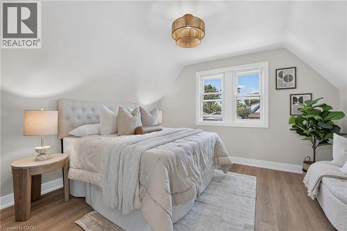 Sloped ceiling architectural detail, wood-finish flooring, white trim windows, and a built-in upholstered headboard - 215 Paling Avenue, Hamilton, ON 