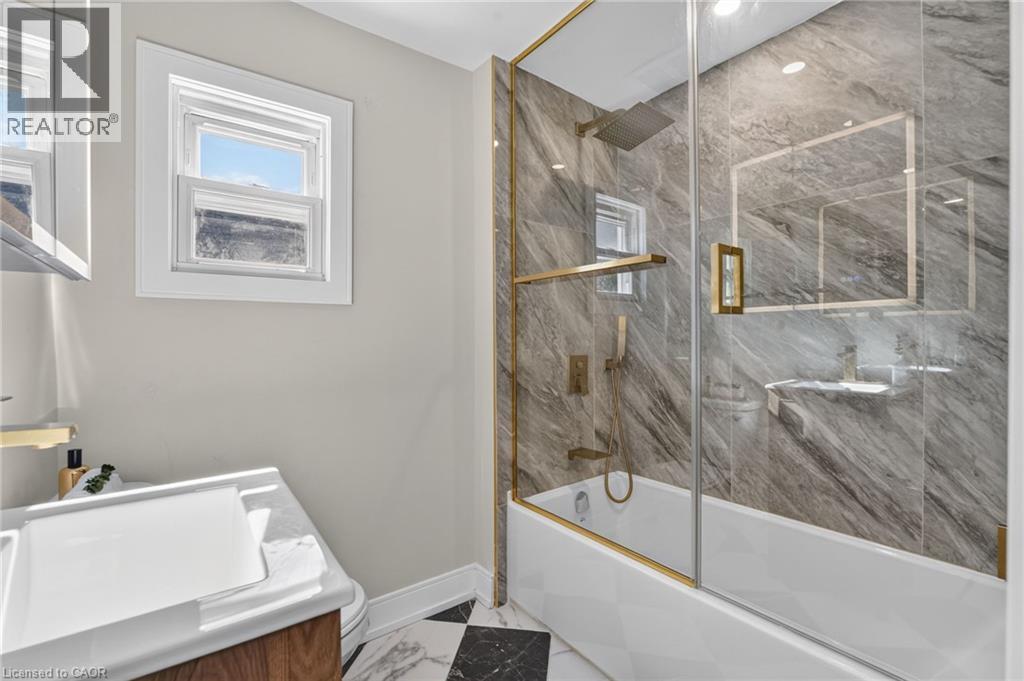 Built-in bathtub with glass enclosure, gold-finish fixtures, and full-height stone-look tile surround - 215 Paling Avenue, Hamilton, ON