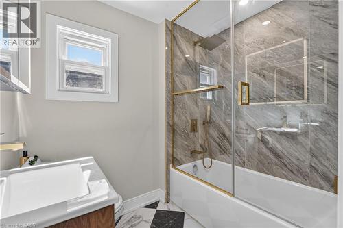 Built-in bathtub with glass enclosure, gold-finish fixtures, and full-height stone-look tile surround - 215 Paling Avenue, Hamilton, ON 