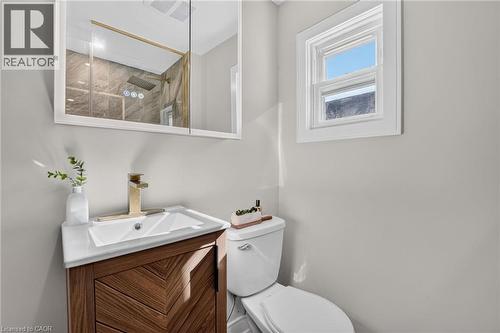 Vanity with a white basin and gold-finish faucet, framed mirror, and a window - 215 Paling Avenue, Hamilton, ON 
