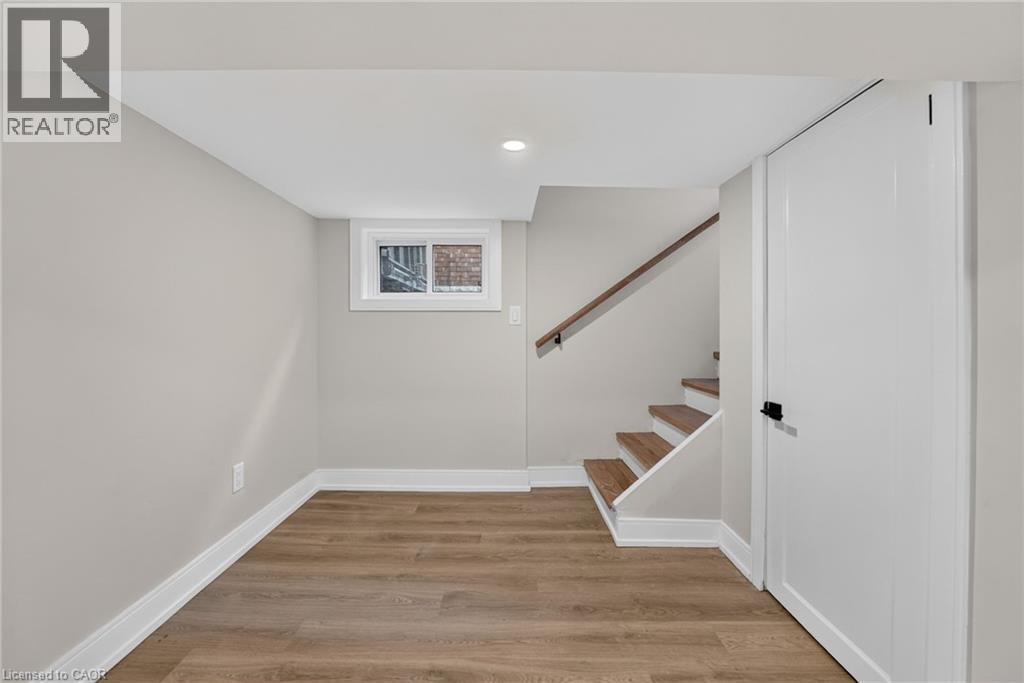Wood-finish flooring, white trim, recessed lighting, white panel door with black hardware, and wood-finish staircase - 215 Paling Avenue, Hamilton, ON