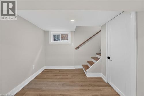 Wood-finish flooring, white trim, recessed lighting, white panel door with black hardware, and wood-finish staircase - 215 Paling Avenue, Hamilton, ON 