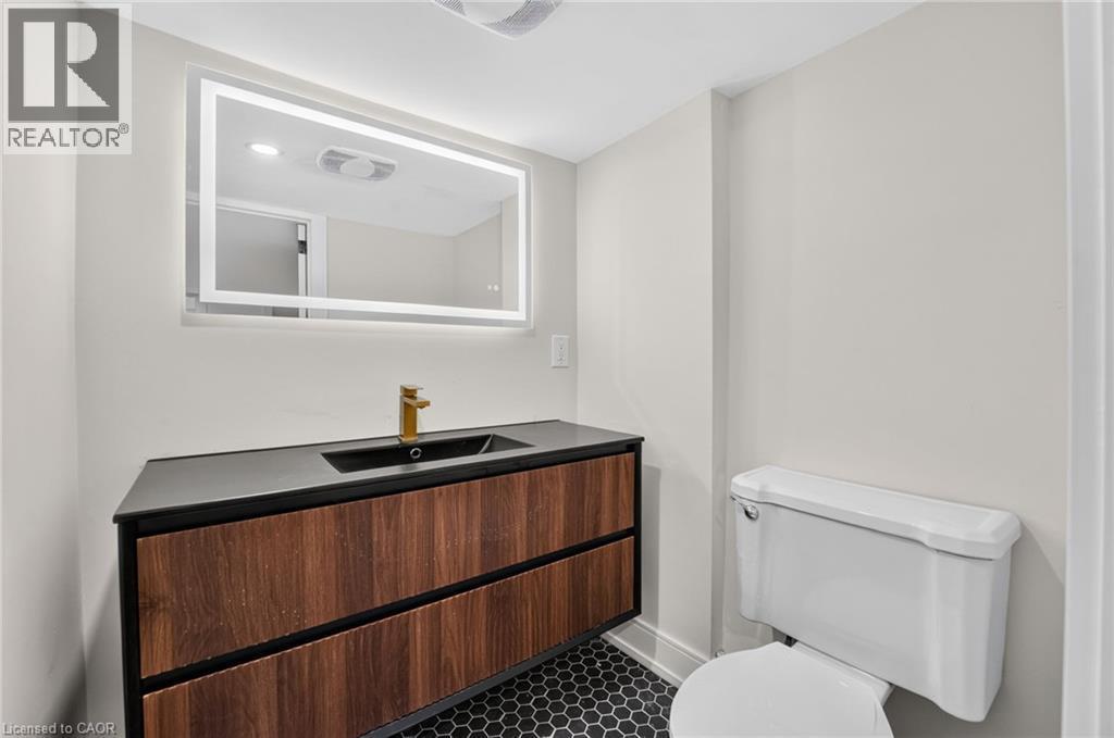 Backlit vanity mirror, wood-finish floating vanity with two drawers, black countertop with integrated sink, and hexagon tile flooring - 215 Paling Avenue, Hamilton, ON