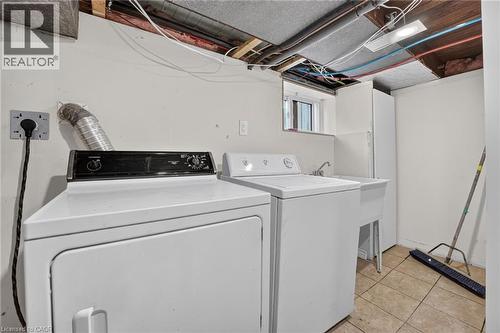 Laundry area featuring tile flooring, a utility sink with a faucet, and a wall-mounted light fixture - 215 Paling Avenue, Hamilton, ON 