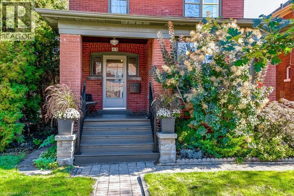 Brick exterior featuring a covered porch, wood-finish steps, stone-clad railing posts, and a paved walkway - 43 Rosslyn Avenue S, Hamilton, ON