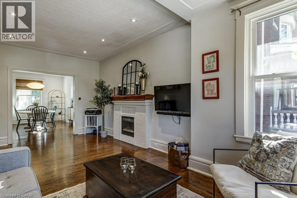 Warm wood-finish flooring complements the white brick fireplace and mantel - 43 Rosslyn Avenue S, Hamilton, ON