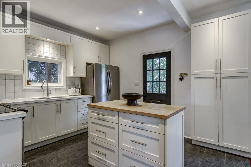 Kitchen featuring white shaker-style cabinetry, a central island with a wood-finish countertop, stainless steel appliances, and a tiled backsplash - 43 Rosslyn Avenue S, Hamilton, ON