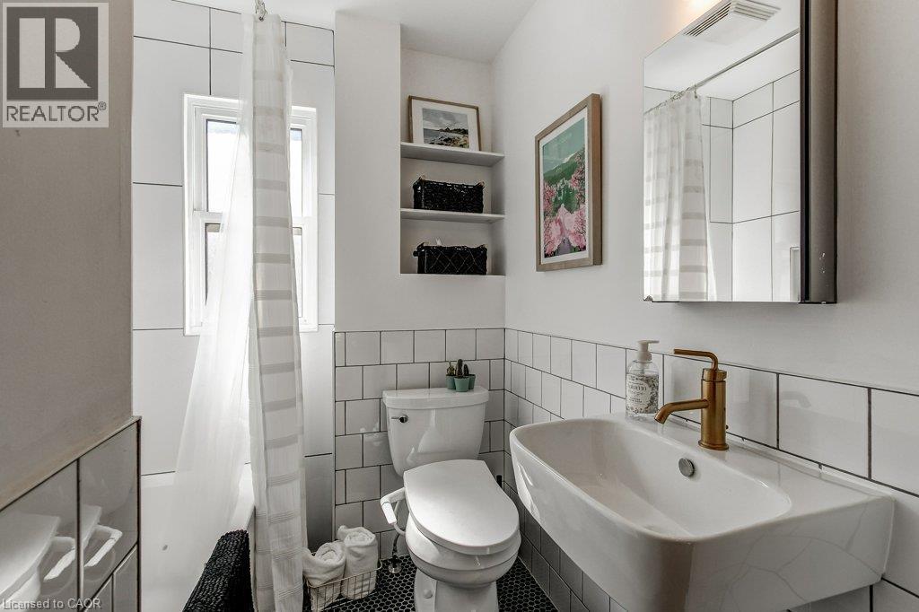 Bathroom featuring white subway tile, a wall-mounted sink with a gold-tone faucet, and an integrated bathtub - 43 Rosslyn Avenue S, Hamilton, ON