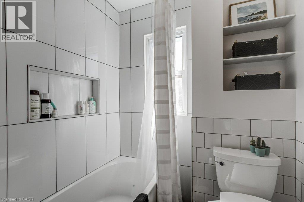 Bathtub with a tiled surround featuring a recessed niche, vertical and horizontal tile patterns, and a window - 43 Rosslyn Avenue S, Hamilton, ON