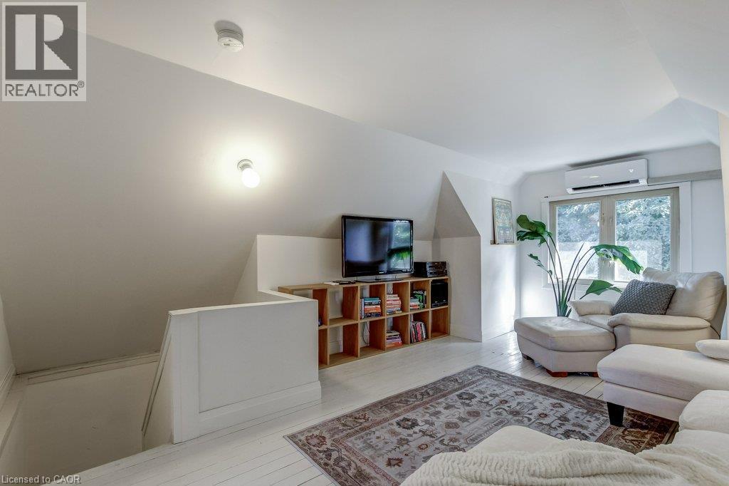 Sloped ceilings, wood-finish flooring, shelving, window with exterior landscaping, and a wall-mounted climate control unit - 43 Rosslyn Avenue S, Hamilton, ON