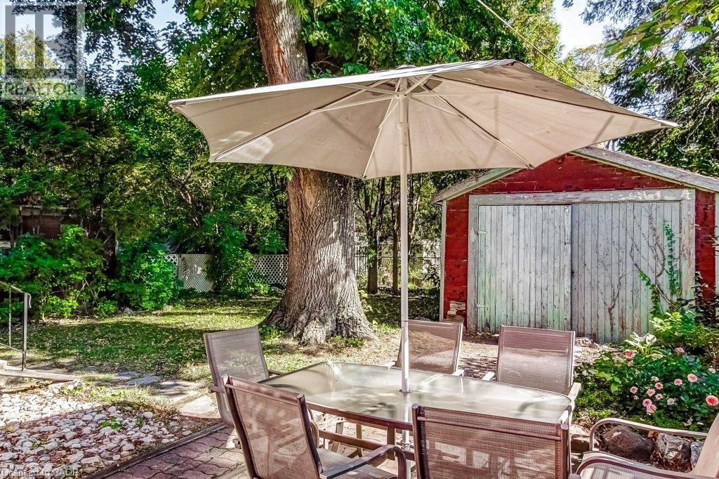 Expansive backyard featuring a red wood-sided garage with double wooden doors, a large mature tree, established plantings, and a paved patio area - 43 Rosslyn Avenue S, Hamilton, ON