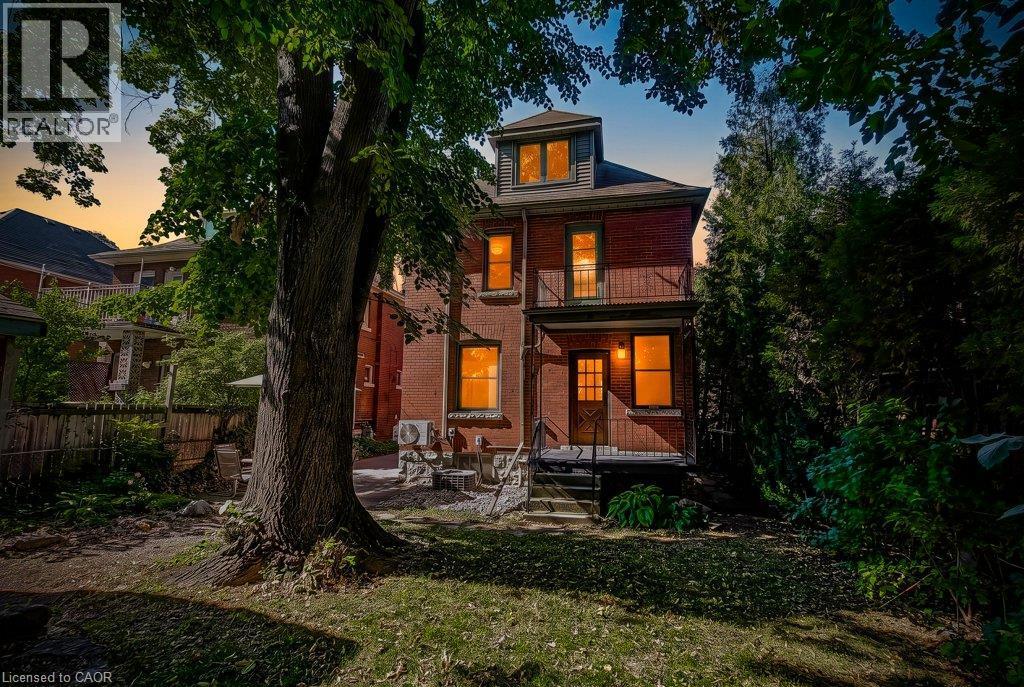 Brick exterior, dormer window, second-story balcony with metal railing, ground-level entrance with metal railing, mature trees - 43 Rosslyn Avenue S, Hamilton, ON