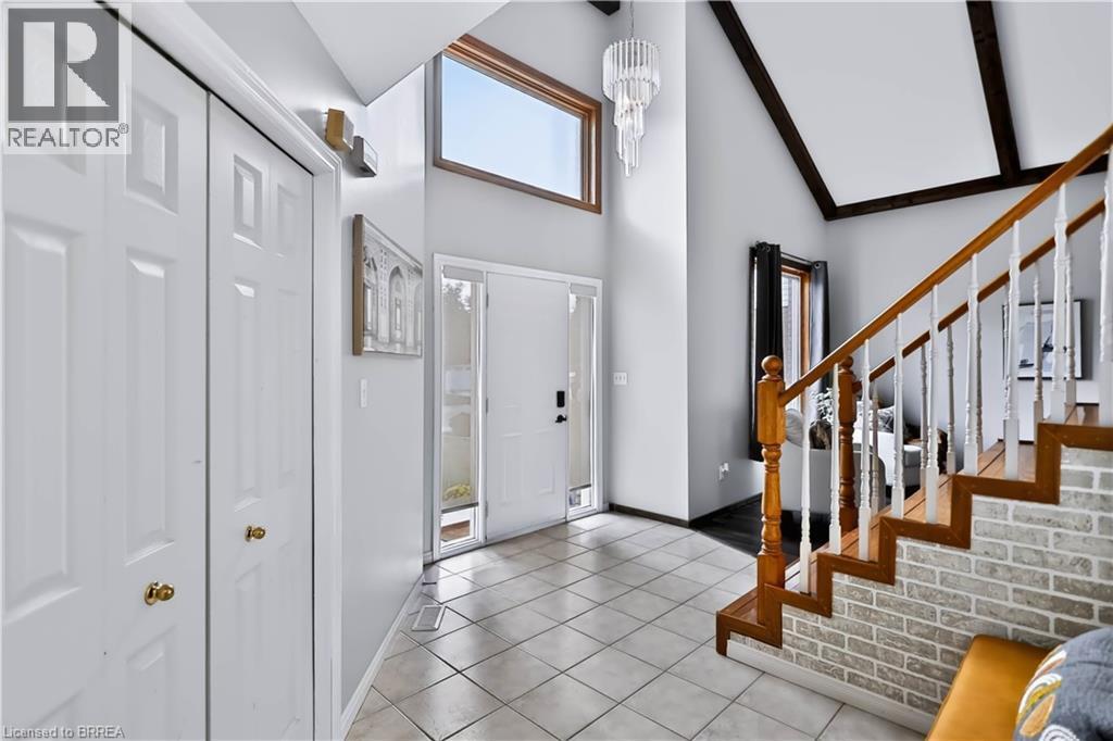 Vaulted ceiling with exposed beams, wood-finish staircase with white balusters, brick-finish staircase wall, tile flooring, and a contemporary chandelier - 19 Hyslop Drive, Caledonia, ON