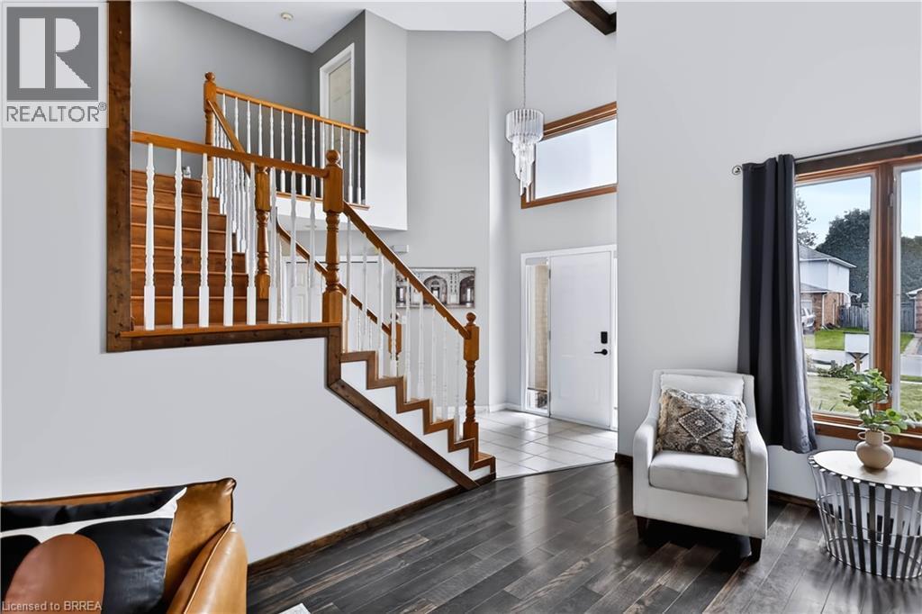 Two-story entry with wood-finish flooring, a traditional staircase with wood handrails, and a transom window above the entry door - 19 Hyslop Drive, Caledonia, ON
