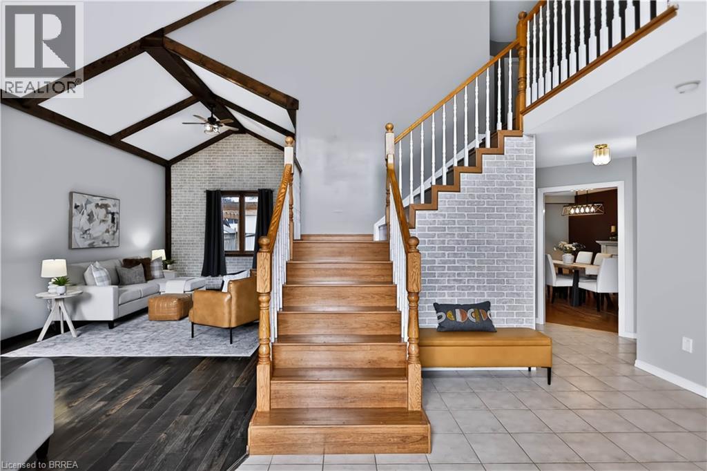 Wood-finish staircase with white balusters, vaulted ceiling with exposed beams, brick accent wall, and dark wood-finish flooring - 19 Hyslop Drive, Caledonia, ON