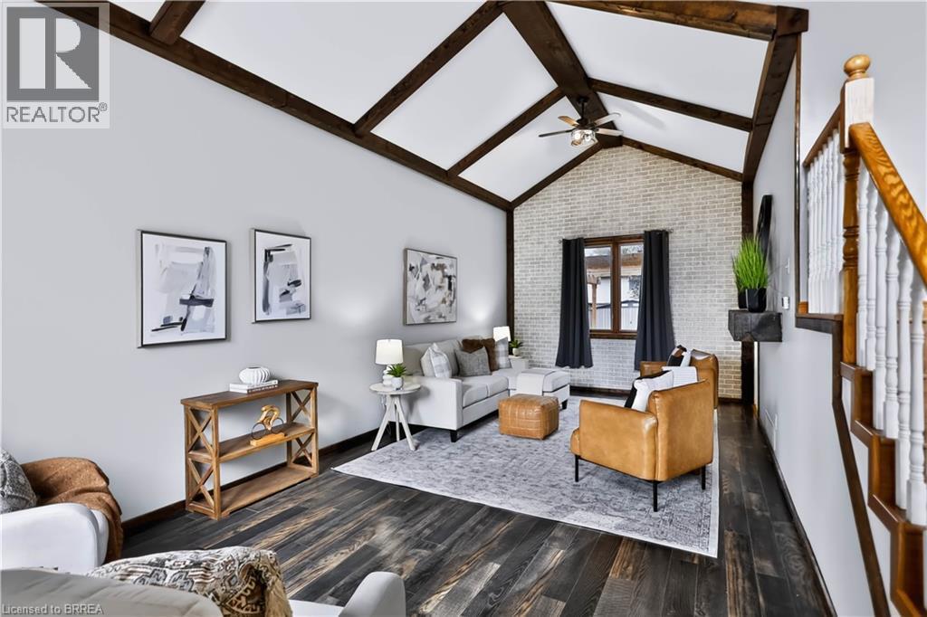 Vaulted ceiling with exposed beams, wood-finish flooring, white painted brick accent wall, ceiling fan, and staircase with wood railing - 19 Hyslop Drive, Caledonia, ON