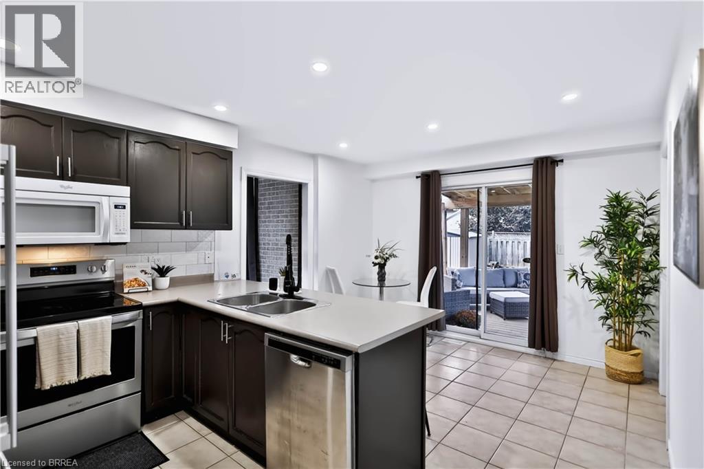 Kitchen featuring dark wood cabinetry, stainless steel appliances, a subway tile backsplash, and light-toned countertops - 19 Hyslop Drive, Caledonia, ON