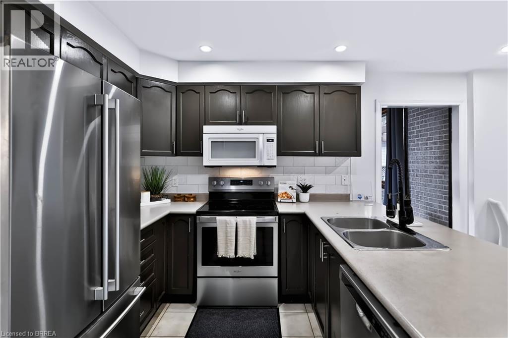 U-shaped kitchen featuring dark wood cabinetry, stainless steel appliances, a subway tile backsplash, light-toned countertops, and recessed lighting - 19 Hyslop Drive, Caledonia, ON
