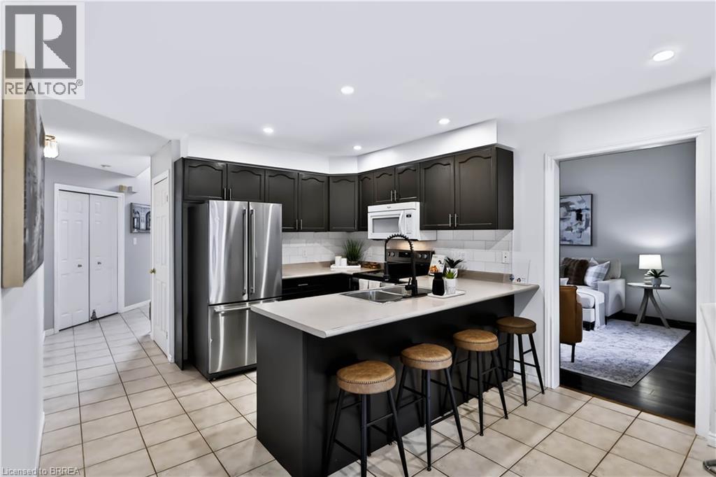 Kitchen featuring dark cabinetry, stainless steel appliances, a white subway tile backsplash, and a light-toned countertop island - 19 Hyslop Drive, Caledonia, ON