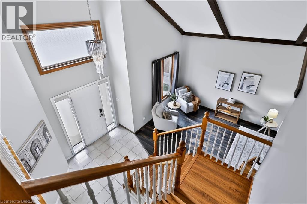 Vaulted ceiling with exposed wood beams, wood-finish flooring, white tiled entryway, natural wood staircase, and a contemporary chandelier - 19 Hyslop Drive, Caledonia, ON