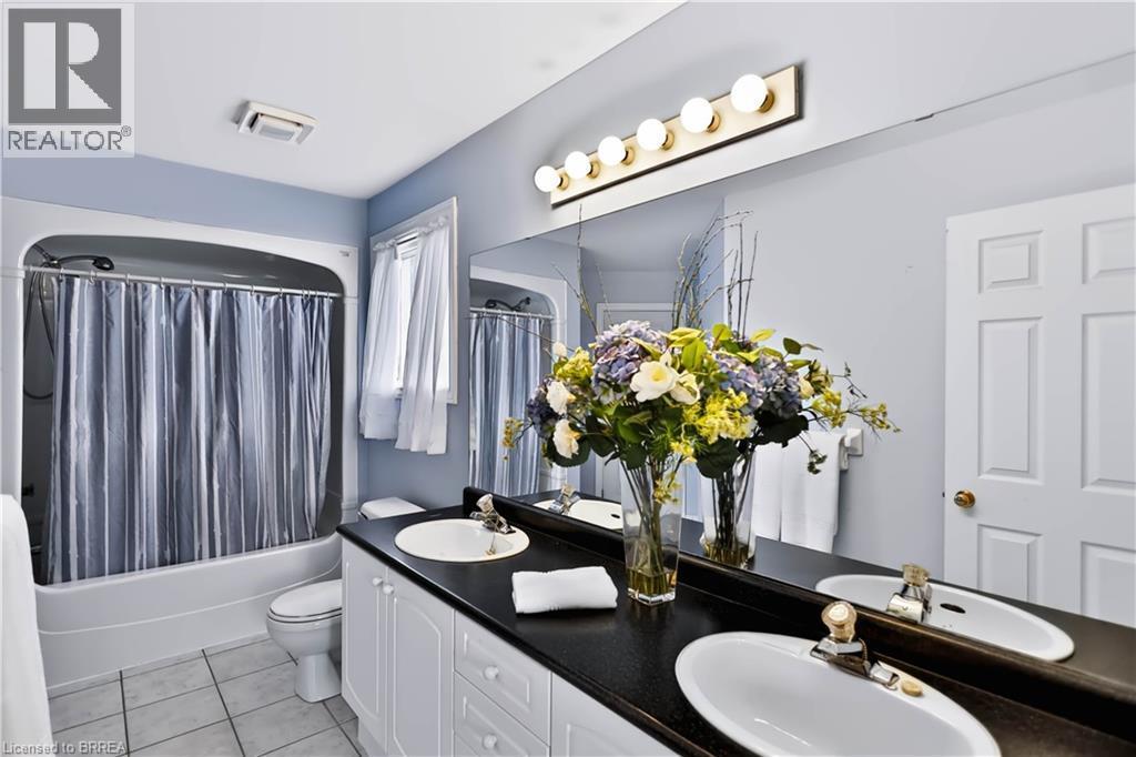 Double vanity with undermount sinks, black countertop, white cabinetry, and large wall-mounted mirror - 19 Hyslop Drive, Caledonia, ON